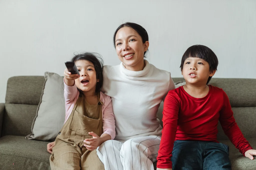 English IPTV: What It Means and Who It Is For Mother watching TV with her two children, holding a remote control